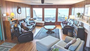 A spacious living room with a large window overlooking a scenic view, furnished with leather sofas, a coffee table, and a bookshelf. - Sparkling Clean, Private & Quiet! Amazing Ocean Views [1] (Brookings)