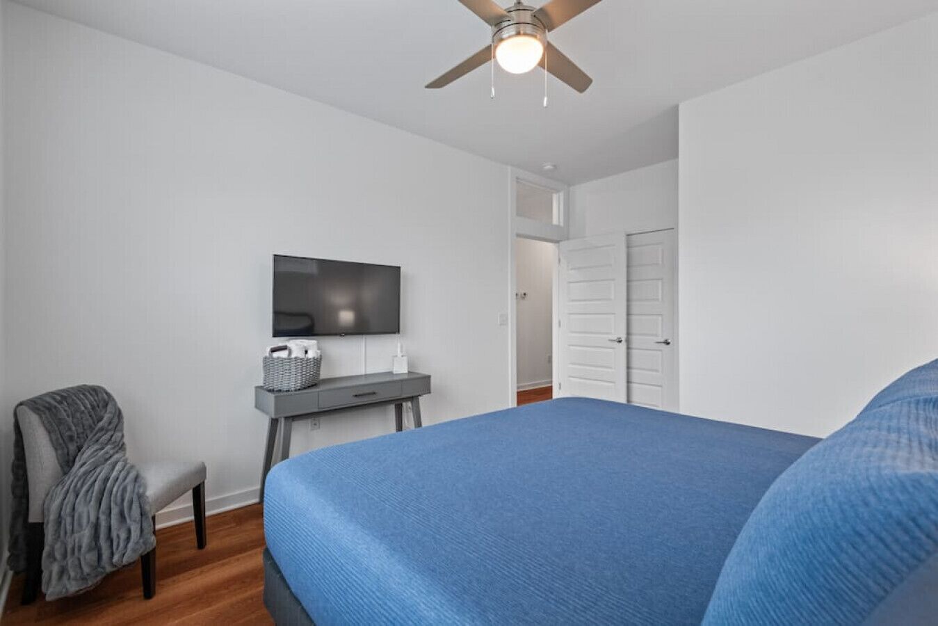 Un dormitorio con cama, escritorio, silla, televisor y ventilador de techo.