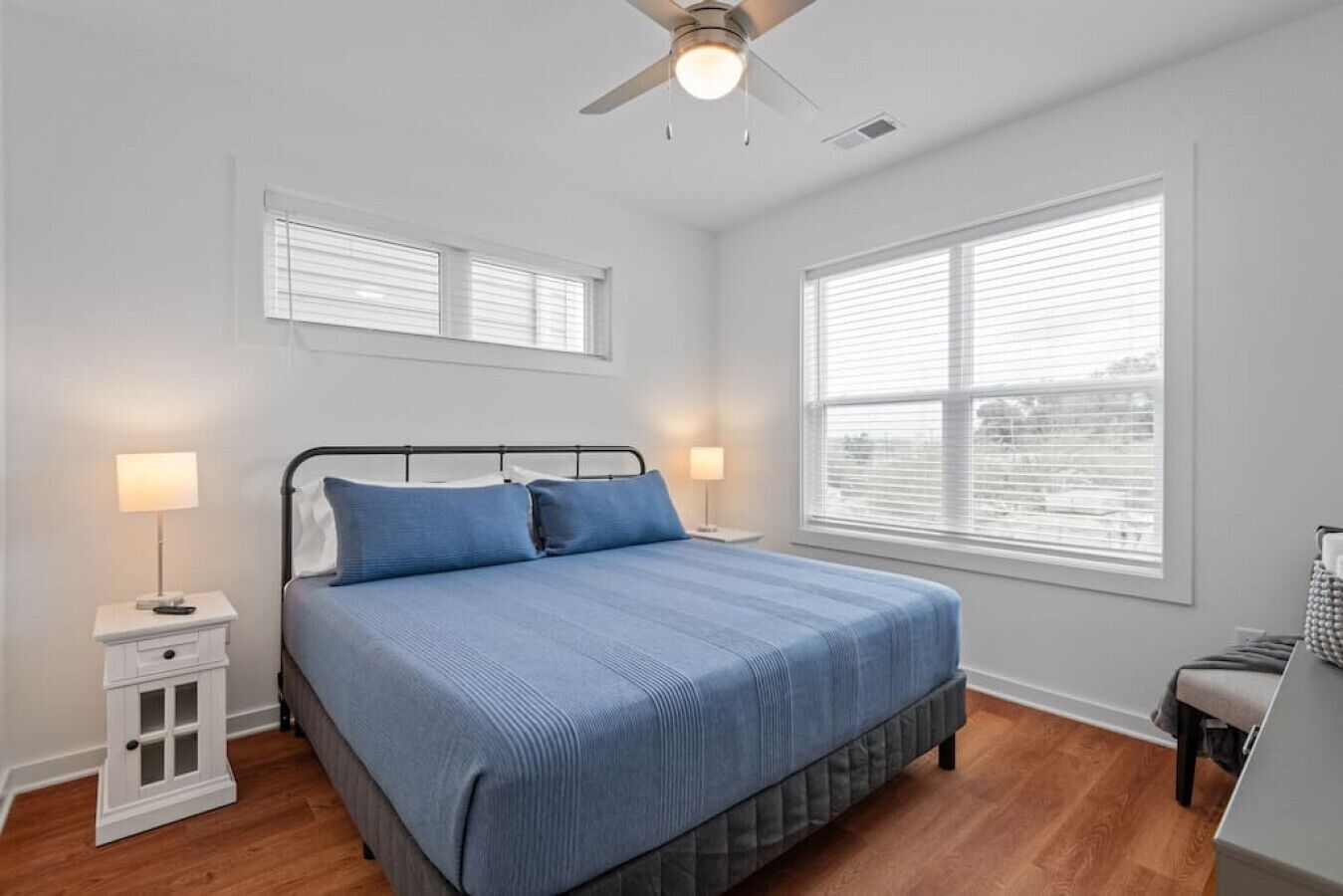 A bedroom with a bed, bedside tables, a ceiling fan, and large windows.