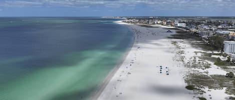 Une plage cĂŽtiĂšre offrant une vue dĂ©gagĂ©e sur lâocĂ©an, avec un rivage sablonneux et des bĂątiments situĂ©s Ă proximitĂ©.