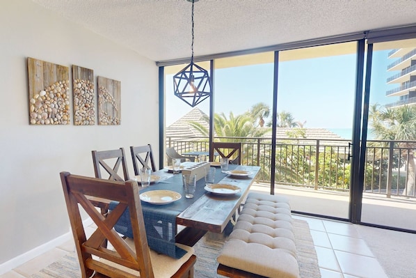 A dining area with a long table, chairs, and a view of the ocean through large windows.