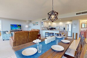 A modern kitchen with white cabinets, a stainless steel refrigerator, and a dining area with a wooden table set for four.
