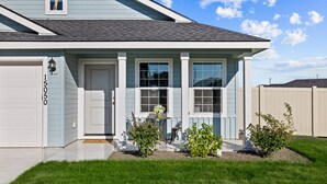 A residential house with a light blue exterior, a white garage door, and a front porch with a small table and potted plants.