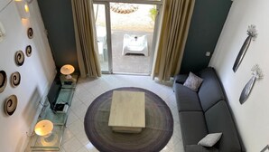 Ein modernes Wohnzimmer mit einer Couch, einem Couchtisch und einem Glastisch mit einer Lampe. Ein Schiebetür aus Glas führt in einen Außenbereich.