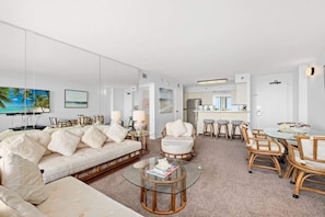 Uma sala de estar moderna com um sofá, cadeiras, uma mesa de centro de vidro e um espaço de refeições com mesa e cadeiras.