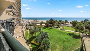 A hotel with a balcony overlooking a beach, a well-maintained lawn, and palm trees. - San Luis Beauty in The Beautiful San Luis Resort Pet Friendly (Galveston)