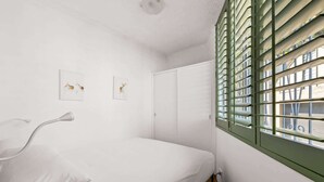 Un dormitorio minimalista con una cama individual, un armario blanco y una ventana con contraventanas verdes.