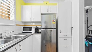 Una cocina compacta con armarios blancos, un refrigerador de acero inoxidable, un microondas y una cafetera.