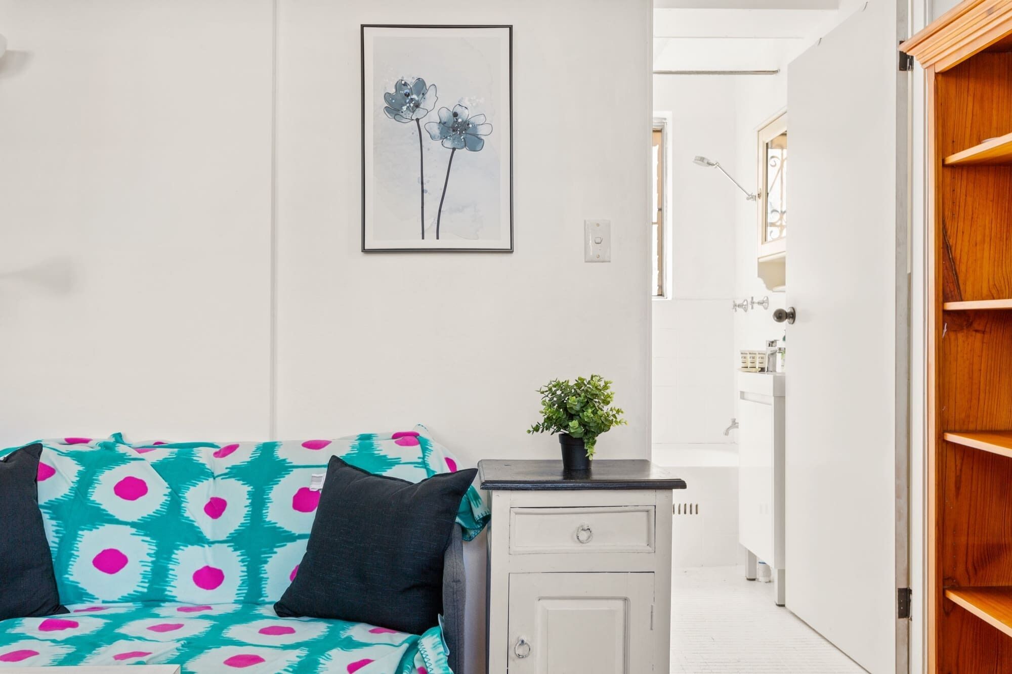 A room with a teal and white patterned sofa, a small white cabinet, and a framed artwork on the wall.