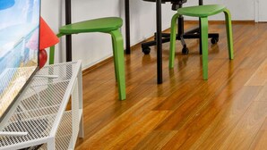 Una habitación con piso de madera, un escritorio con silla, un monitor de computadora y una ventana con persianas.