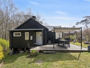 Et sort træhus med terrasse, overdækket veranda og en lille have.