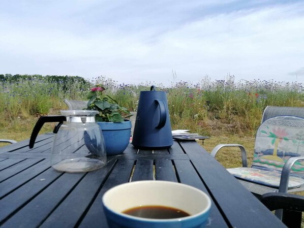 A picnic table with a cup of coffee, a glass jar, a blue mug, and a potted plant.