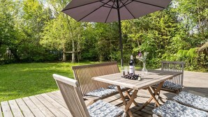 Une terrasse en bois avec une table et des chaises, un parasol et une bouteille de vin.