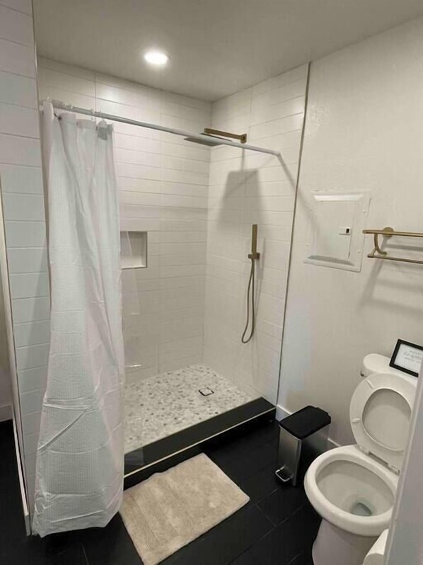 A modern bathroom with a glass-enclosed shower, a toilet, and a small sink.