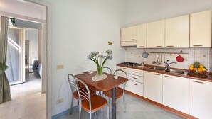 A compact kitchen with white cabinets, a wooden dining table, and a small countertop with fruit. - Casa Milli C: A cozy apartment situated on a promontory facing the sea. (Massa Lubrense)
