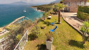 A coastal property with a stone building, a grassy lawn, and a view of the sea. - Casa Milli C: A cozy apartment situated on a promontory facing the sea. (Massa Lubrense)