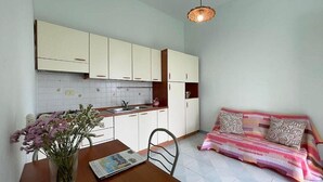 A compact kitchen with white cabinets, a dining table with a vase of flowers, and a sofa with patterned cushions. - Casa Milli C: A cozy apartment situated on a promontory facing the sea. (Massa Lubrense)