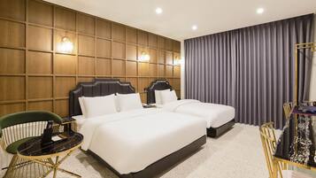 A hotel room with two beds, a green chair, a small round table, and a large window with curtains.