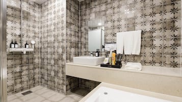 A modern bathroom with patterned tiles, a large mirror, a bathtub, and a vanity with toiletries.