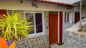 Una casa de piedra con un pequeño porche, una ventana con cortina morada y una puerta roja.