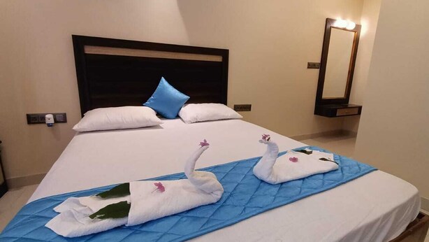 Habitación de hotel con cama, cubrecama azul y dos toallas con forma de cisne adornadas con flores rosadas.