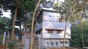 Un edificio de dos pisos con fachada blanca y techo de tejas rojas, rodeado de árboles y una cerca.