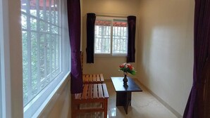 Una habitación con ventana, un banco, una mesa con un jarrón de flores y un ventilador de techo.