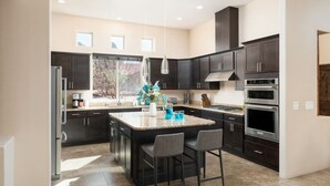 A modern kitchen with dark cabinetry, a central island with bar stools, and built-in appliances. - Two Custom Homes with Pool, Spa, Rooftop Deck (Sedona)