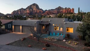 A modern house with a garage, a patio with chairs, and a view of red rock formations in the background. - Two Custom Homes with Pool, Spa, Rooftop Deck (Sedona)