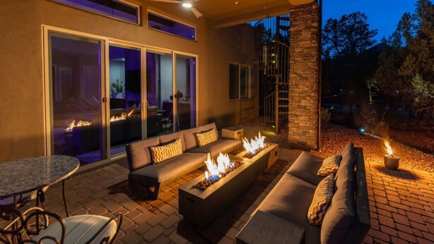 An outdoor living area with a fire feature, seating, and a glass door leading to an interior space. - Two Custom Homes with Pool, Spa, Rooftop Deck (Sedona)