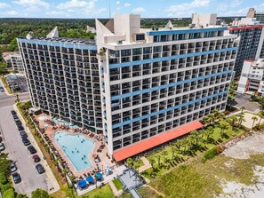 A multi-story hotel with a swimming pool, parking area, and a landscaped garden.