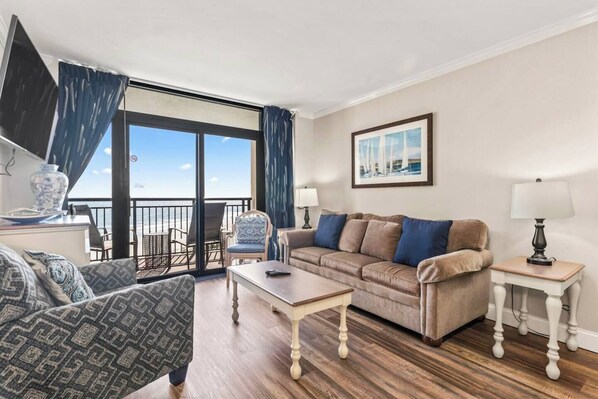 A living room with a sofa, armchairs, a coffee table, and a balcony with a view of the sea.