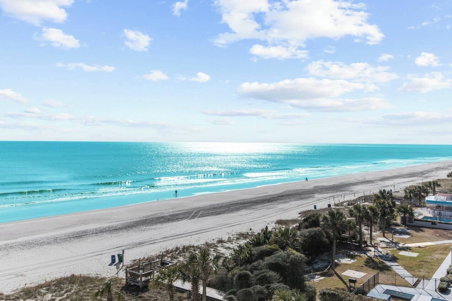 Une plage avec un ciel dégagé, un rivage sablonneux et quelques personnes qui se promènent.