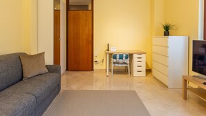 A compact living space with a sofa, a desk with a chair, a TV, and a wardrobe.