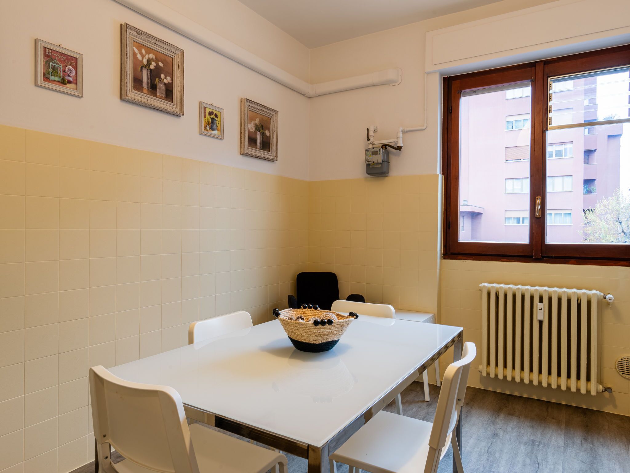 A small dining area with a white table and chairs, a basket of bread, and a window with a view of buildings.