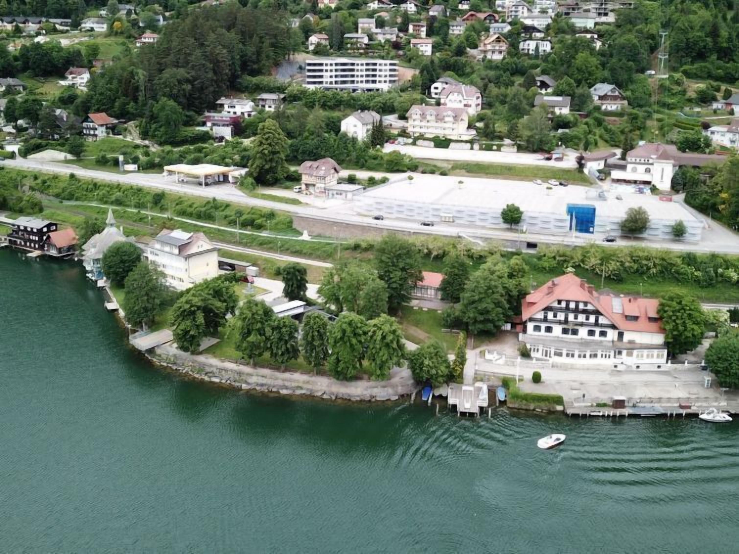 Vista aérea de una propiedad frente al lago con un muelle, un edificio grande de techo rojo y vegetación circundante.