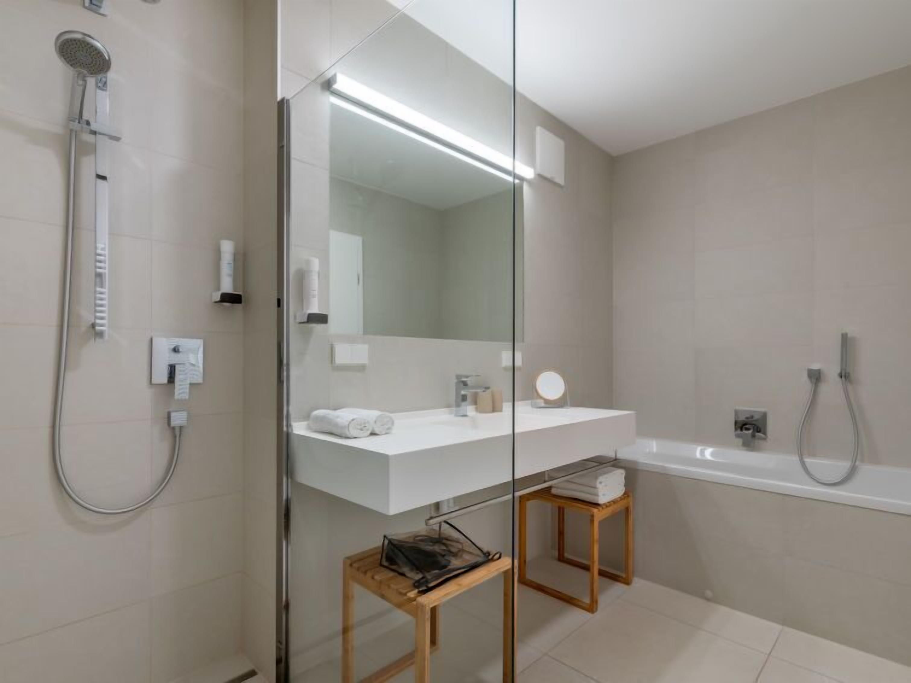 A modern bathroom with a glass shower enclosure, a white vanity with a mirror, and a separate bathtub.