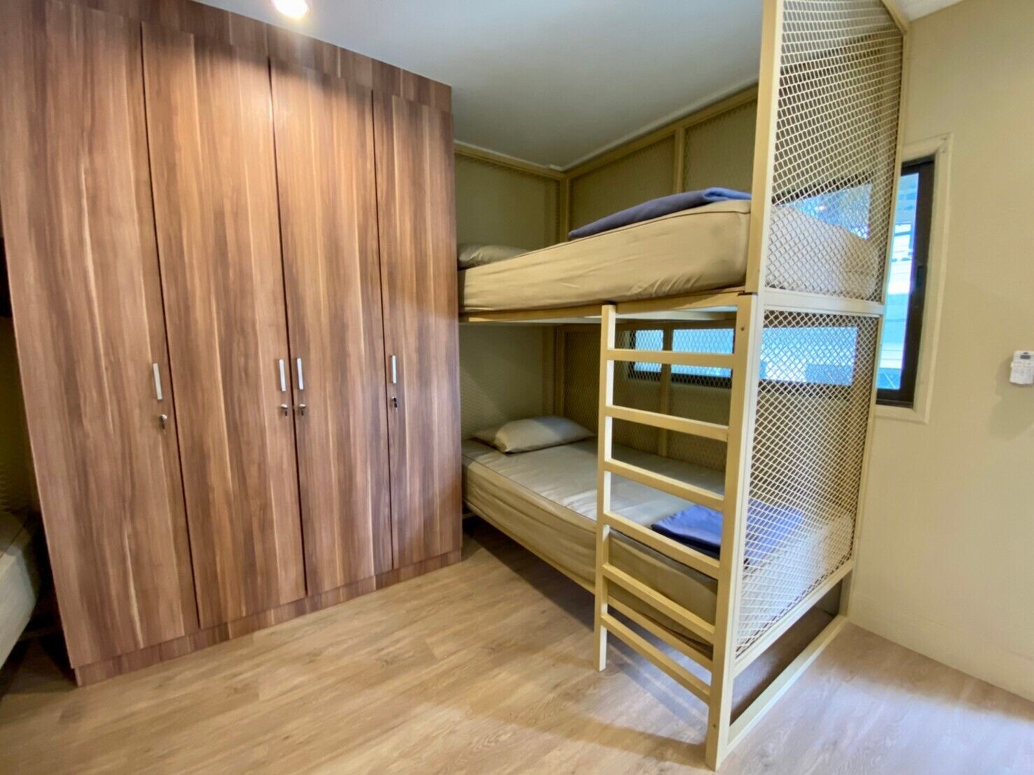 A compact room with a bunk bed, a wooden wardrobe, and a window.