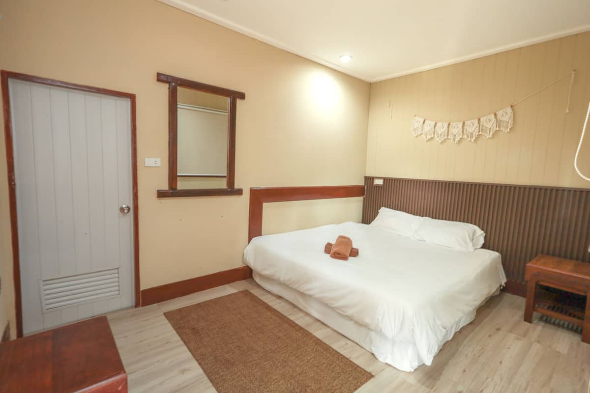Quarto com cama, cabeceira de madeira, mesa de cabeceira, espelho e porta.