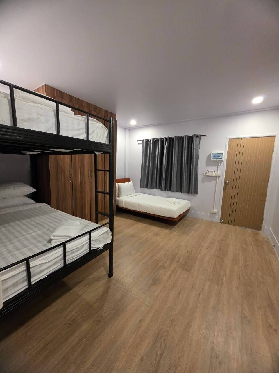 Una habitación con literas, una cama individual, suelo de madera, un armario, una cortina y una puerta.