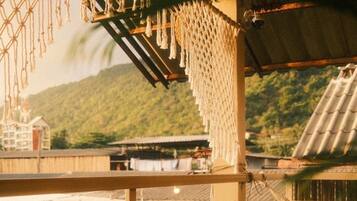 A covered outdoor seating area with wooden tables and chairs, overlooking a mountainous landscape.