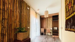 A room with a bamboo wall, a wooden bench with a plant, a desk with a chair, and a hanging light fixture. - Notting Hill Gusethouse (Ko Pha-ngan)