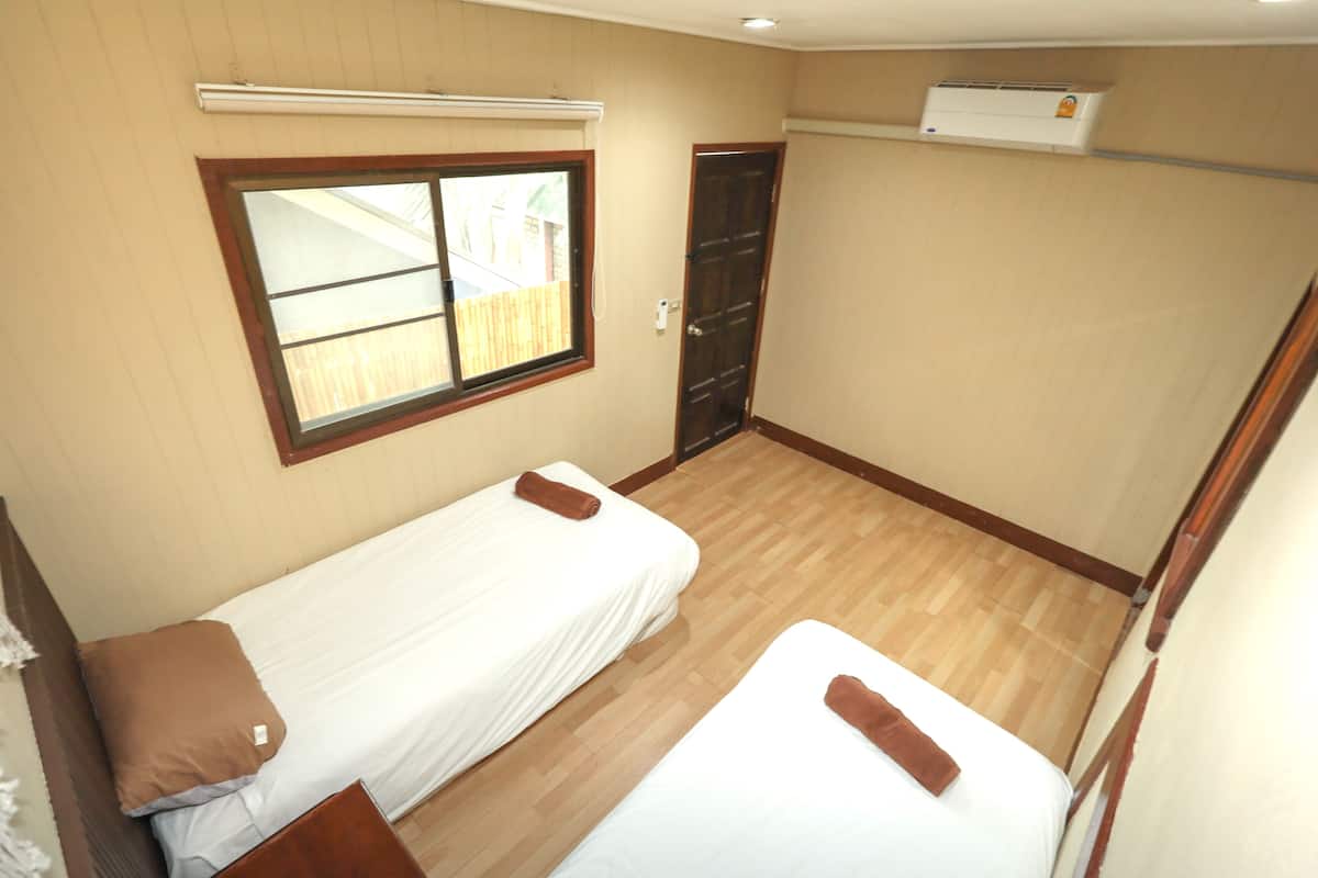 Quarto pequeno com duas camas de solteiro, uma janela, uma porta e aparelho de ar condicionado.