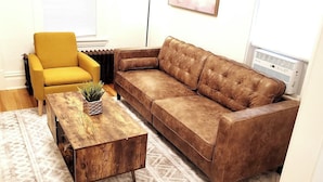 Ein Wohnzimmer mit einer braunen Ledersofa, einem gelben Sessel und einem Couchtisch aus Holz mit einer Pflanze.