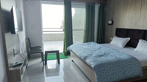 A modern hotel room with a large bed, a flat-screen TV, a bench, and a balcony with green curtains.