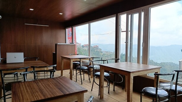 A restaurant with wooden tables and chairs, large windows with a mountain view.