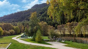 Un parc avec un sentier sinueux, des tables de pique-nique et un petit bâtiment, le tout entouré d’arbres et de collines.