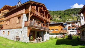 Un chalet en bois, avec des fondations en pierre, un balcon et une vue sur les montagnes.