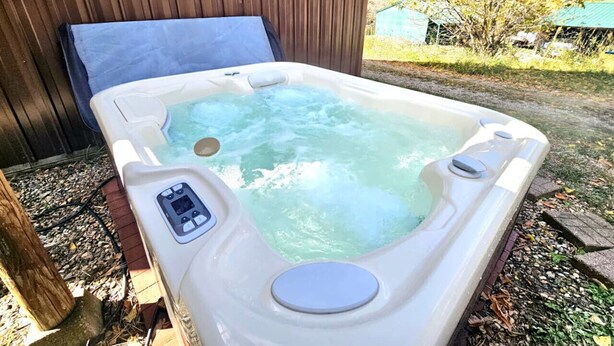 Un jacuzzi con panel de control, rodeado por una terraza de madera y un muro de madera.