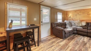 Una habitación acogedora con un sofá de cuero marrón, una pequeña mesa de madera con dos taburetes y una ventana con persianas.